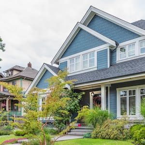 A blue luxury suburban house with gray roof and white trim and green landscaping